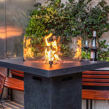 Elementi Montreal Bar Table in Dark Gray showcasing its blazing flames with the optional windscreen