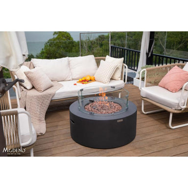 The Venice Round Fire Pit by Modeno in black placed outdoors with couches around